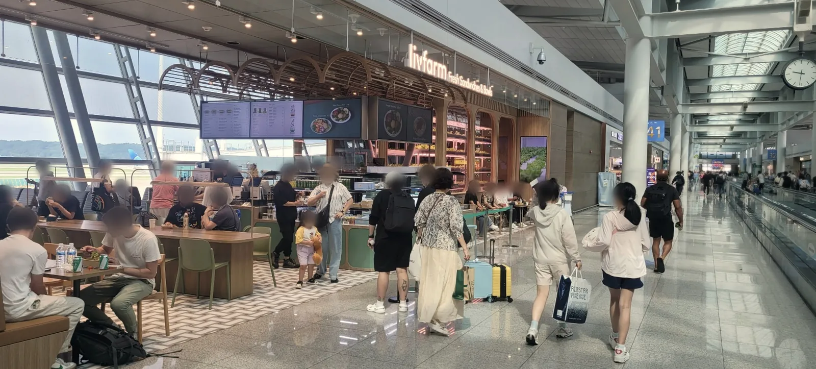 인천공항 제1여객터미널 41번 게이트 근처의 livfarm 매장. 메뉴 화면과 재배 선반이 있는 매장 앞에서 손님들이 식사하고 여행객이 지나갑니다 (사람 얼굴은 흐리게 처리)